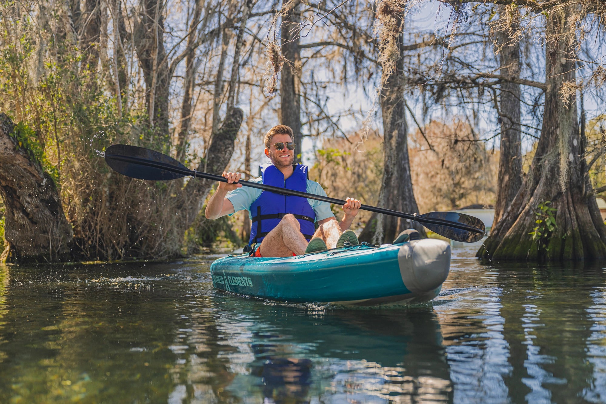 Man kayaking through a forest landscape with an Advanced Elements kayak during an outdoor adventure
