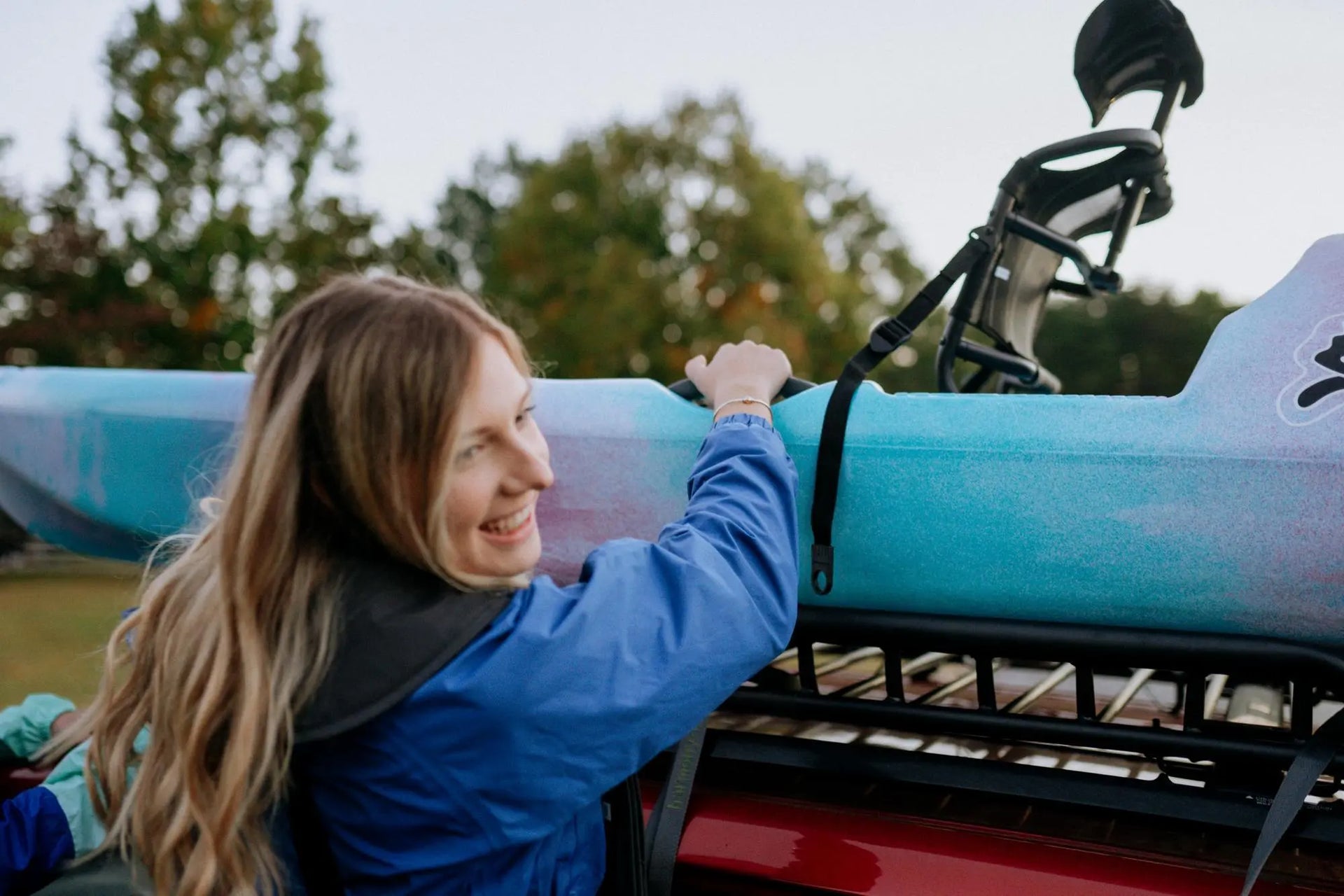 A smiling woman loading a light blue Perception Hangtime 11.5 kayak onto a vehicle roof rack.