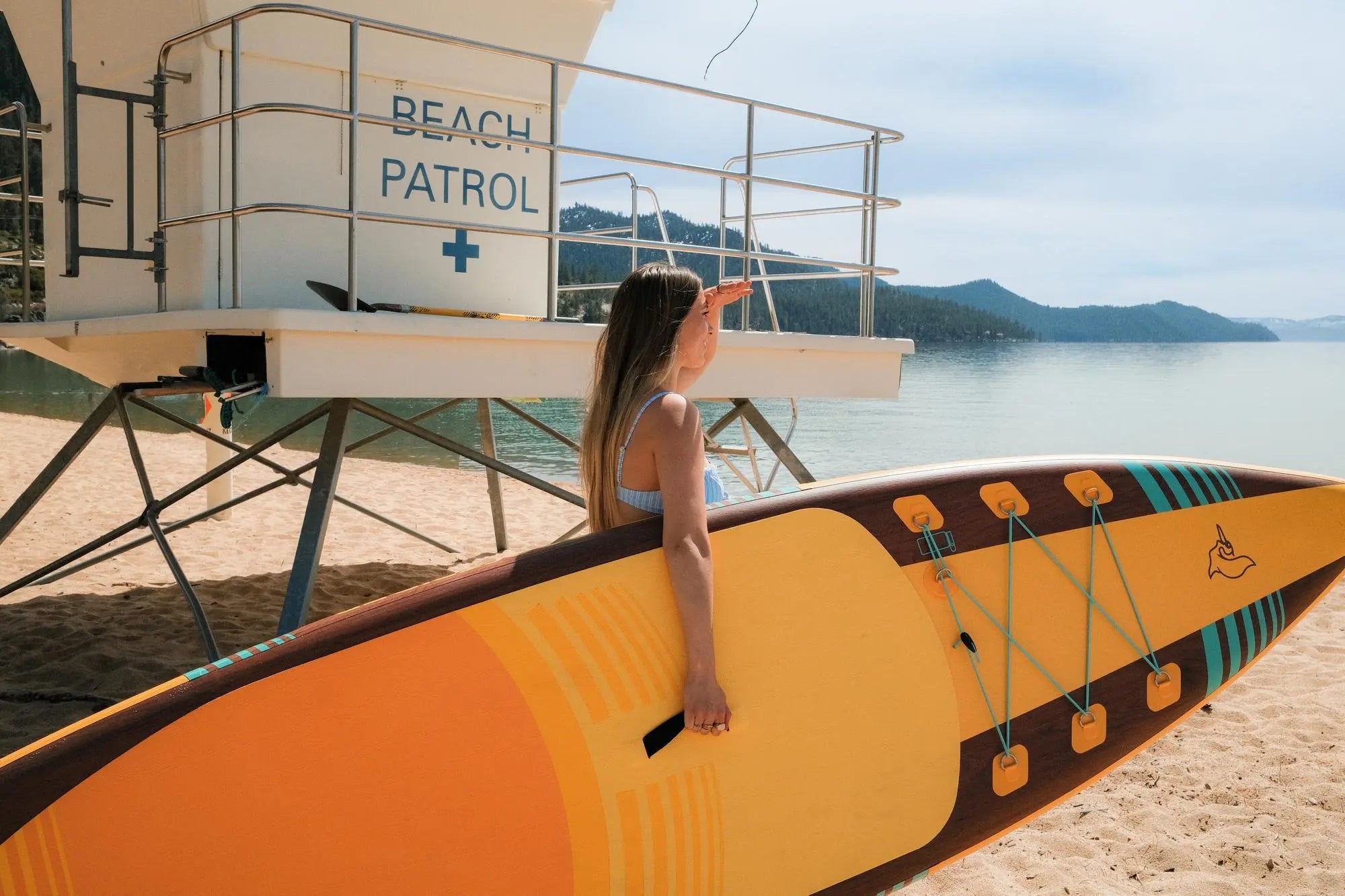 Young woman on the beach holding a Pelican paddle board by the water