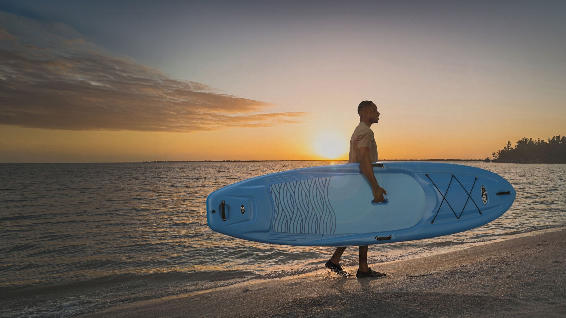 Man holding a Pelican paddle board on the beach at sunset 