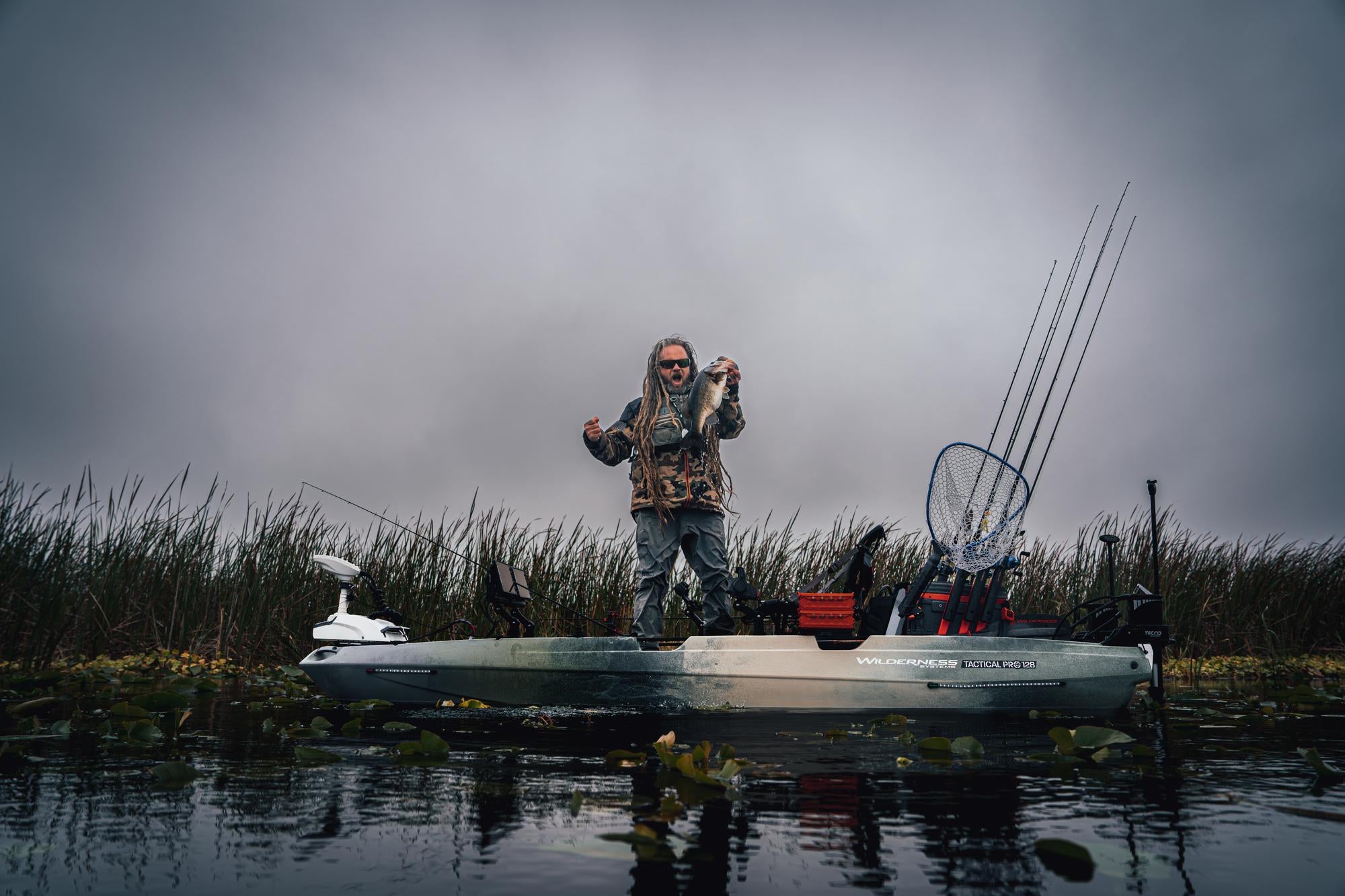 Happy man holding a fish on his Wilderness Systems fishing boat during an outdoor fishing adventure